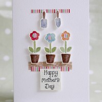 3 small flowers sitting in plant pots with garden tools hanging above